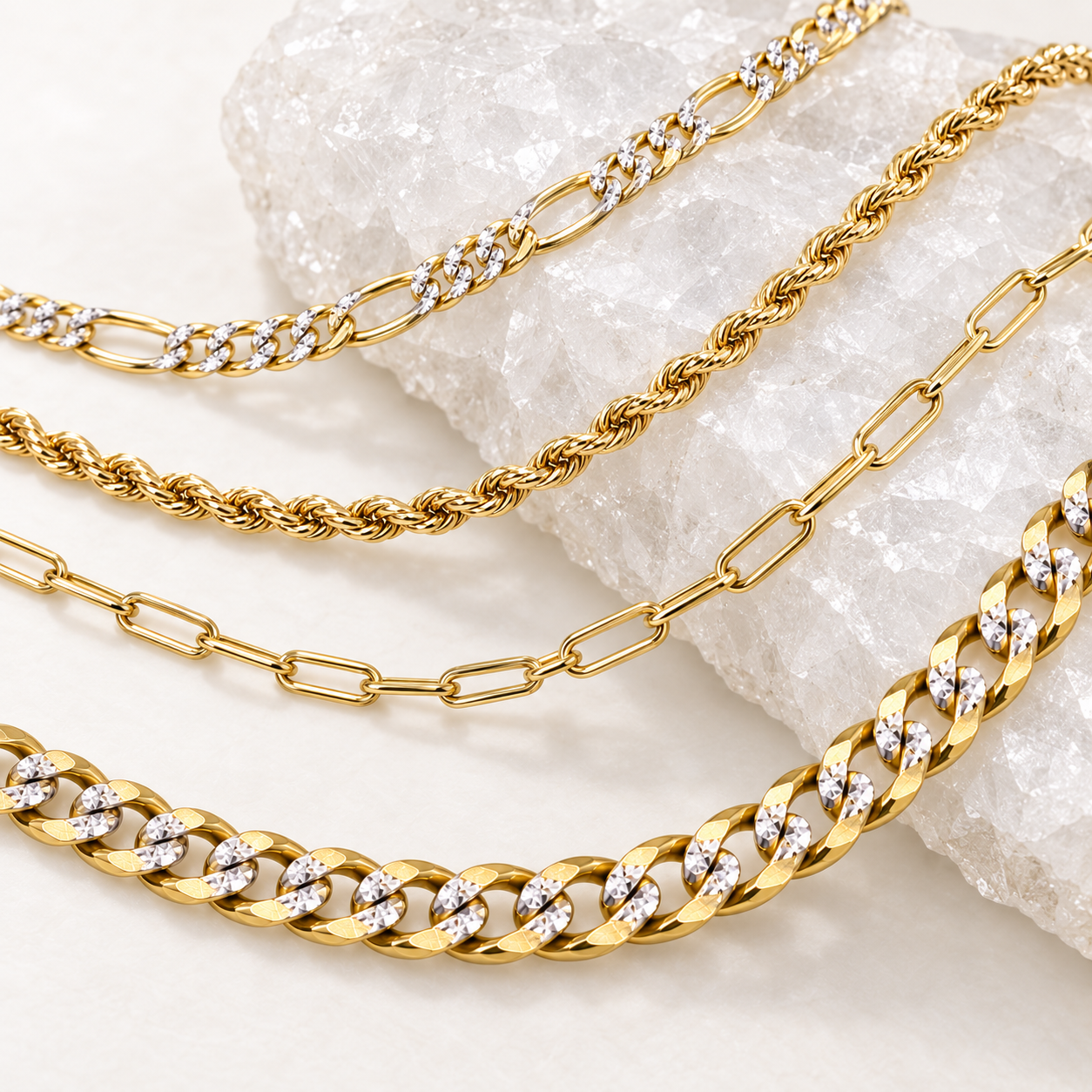 Collection of 14K solid gold Figaro, rope, paperclip and Cuban link chains displayed over clear white crystal