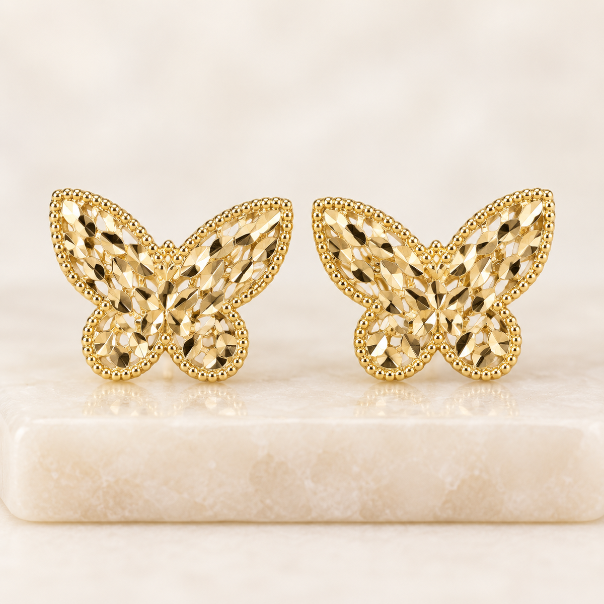     14K yellow gold butterfly stud earrings displayed on an ivory crystal pedestal