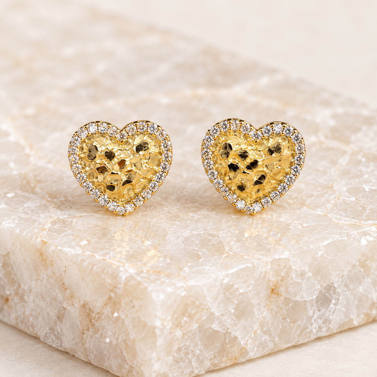 Pair of 13mm 14K solid gold heart nugget stud earrings displayed on a light natural crystal tile