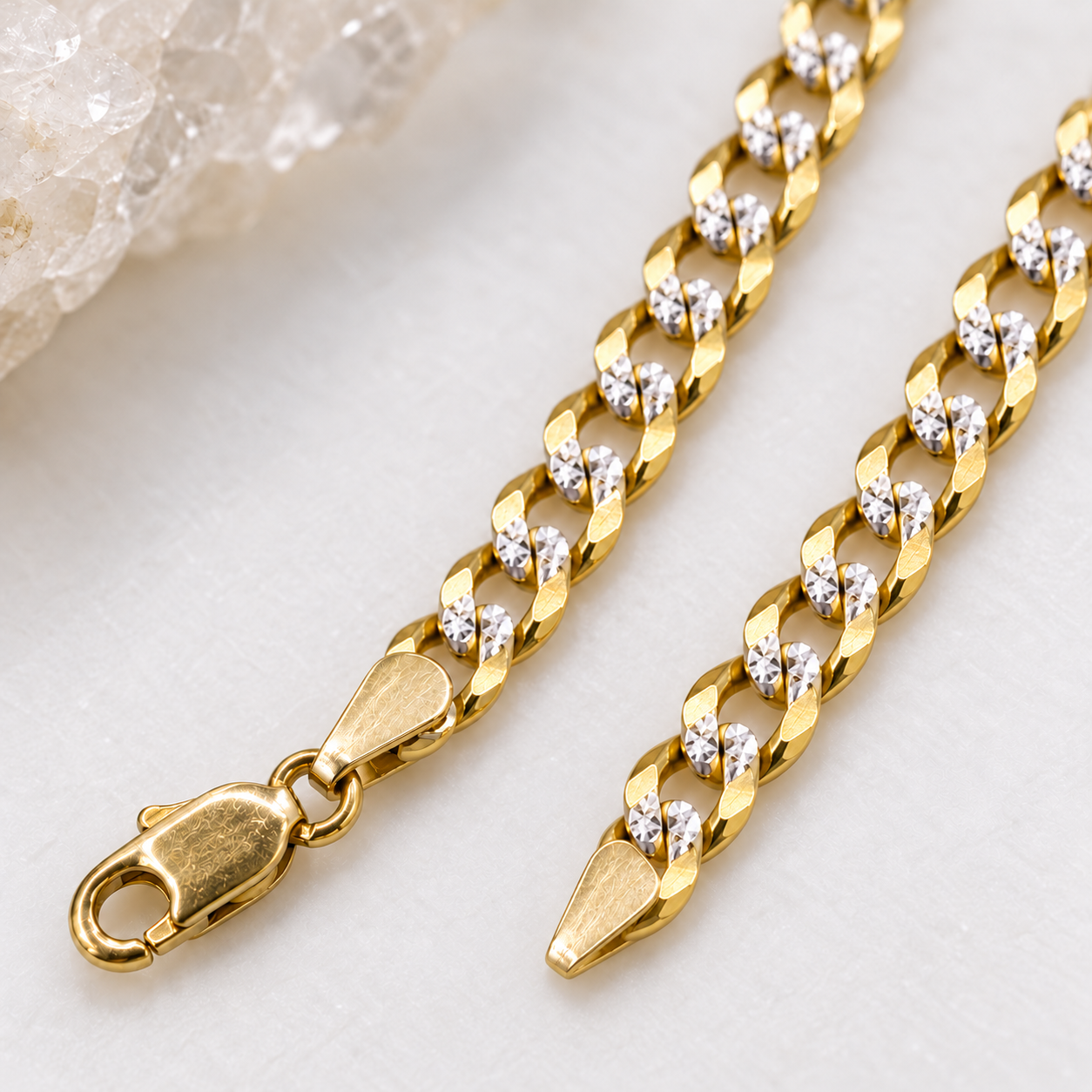Close-up of the small lobster clasp and tapered end terminal on a 14K solid two-tone gold Cuban link chain