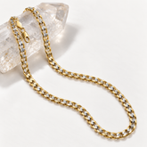14K solid two-tone gold Cuban link chain with diamond-cut accents displayed over clear crystal