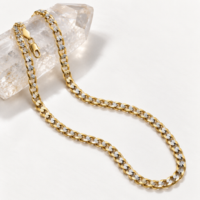 14K solid two-tone gold Cuban link chain with diamond-cut accents displayed over clear crystal